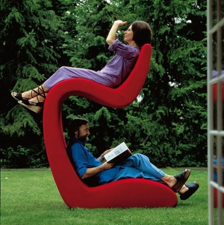 Two people relaxing in a bold red sculptural S-shaped chair outdoors, representing the creative, unconventional choices writers make during the book revision process