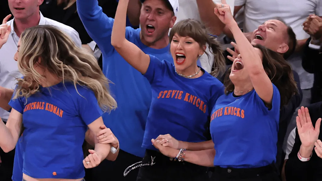 Taylor Swift and a crowd cheer enthusiastically in the stands wearing blue New York Knicks-themed t-shirts that read "STEVIE KNICKS" and "NICKOLE KIDMAN." This playful sports and pop-culture mashup illustrates how embracing your own unexpected instincts forms the foundation of an authentic, recognizable writing style.